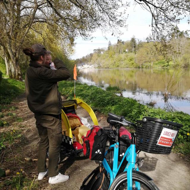 Un papa tient son enfant dans les bras sur le chemin de halage et lui montre la rivière