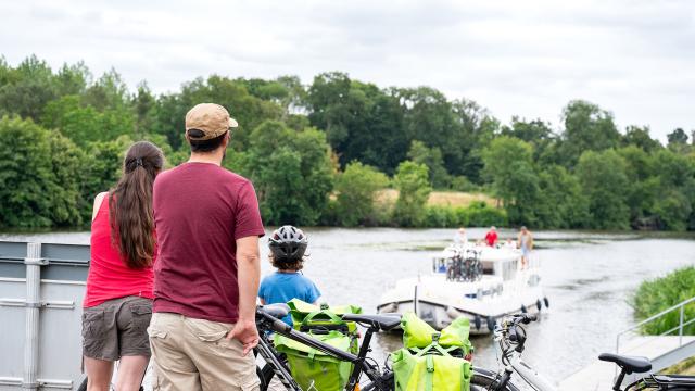 Une famille à vélo le long de la Mayenne observe un bateau qui arrive à une écluse