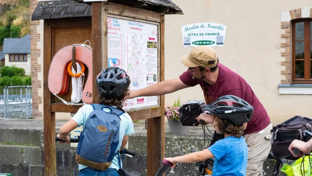 un papa et ses deux enfant regardent un panneau d'information en bord de Mayenne près d'une écluse