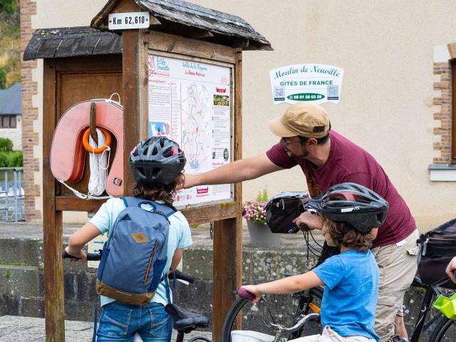 un papa et ses deux enfant regardent un panneau d'information en bord de Mayenne près d'une écluse