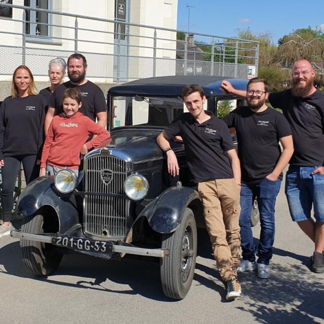 l'équipe de la Coutellerie du Maine Anjou posant appuyé sur une vieille voiture de collection avec la coutellerie en arrière pla