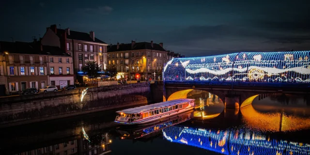 Le bateau Vallis Guidonis navigant de nuit sur la Mayenne. En arrière plan le pont Aristide Briand illuminé par les décoration de Noël