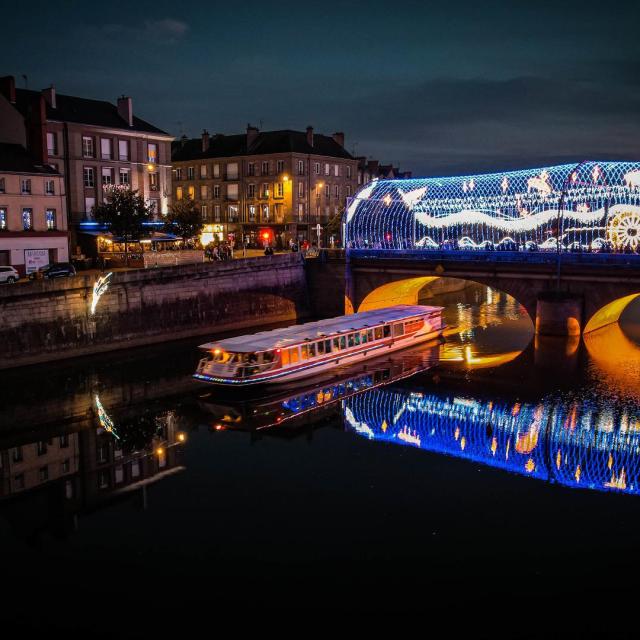 Le bateau Vallis Guidonis navigant de nuit sur la Mayenne. En arrière plan le pont Aristide Briand illuminé par les décoration de Noël