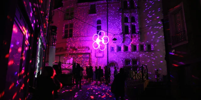 Rue du centre ancien de Laval durant les Lumières de Laval. On y voit une fleur rose lumineuse et une multitude de points colorés