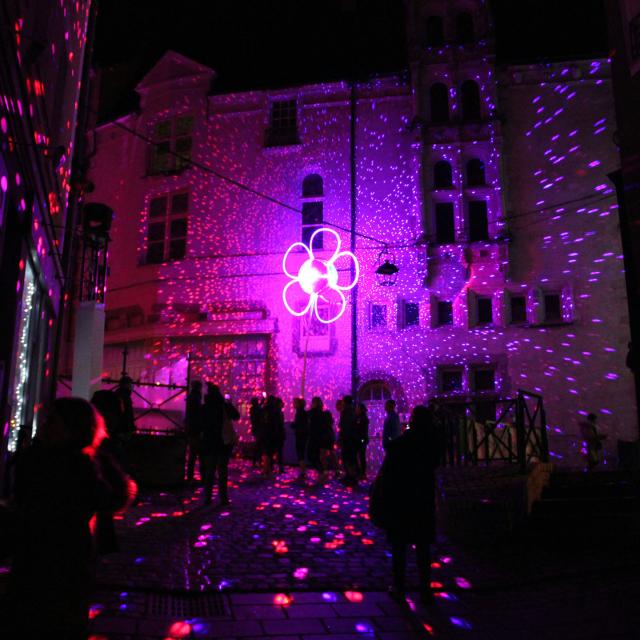 Rue du centre ancien de Laval durant les Lumières de Laval. On y voit une fleur rose lumineuse et une multitude de points colorés