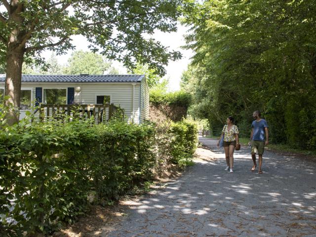 Un couple parcourt les allées du camping de Mayenne à l'ombre des arbres