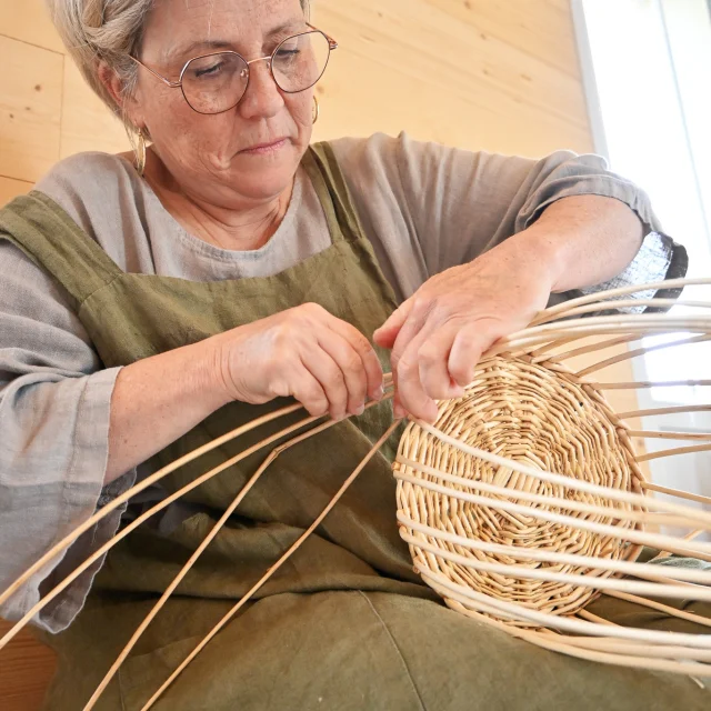 Judith Charpentier en plein travail de tressage de l'osier; Elle n'a pour l'instant que la base de sa création et on voit encore toutes les tiges d'osier qui vont servir à structurer le futur objet.