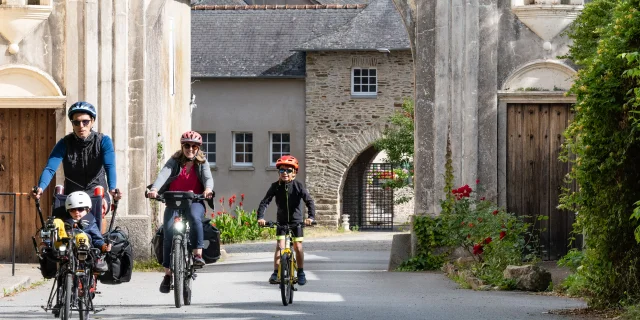 Une famille fait du vélo devant le poche d'entrée de Abbaye Notre Dame du port du Salut à Entrammes