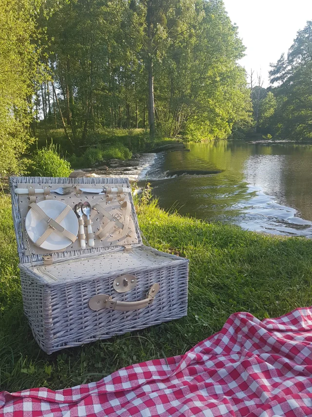 Une nappe vichy et un panier pique nique sont installés au bord de la rivière