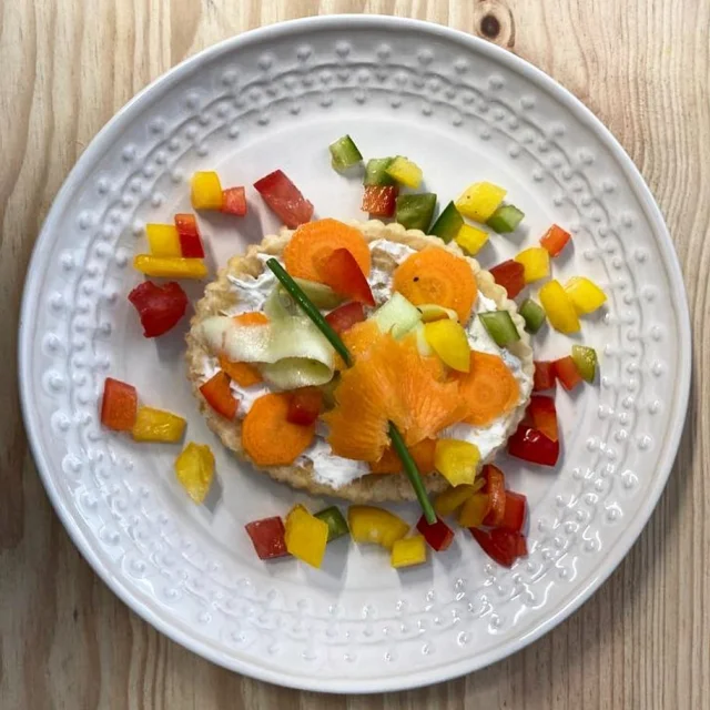 Vue de dessus d'une assiette dans laquelle est dressée une tarte aux légumes crus du restaurant Aux Saisons. Elle est très colorée.