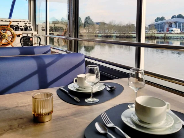 Table de brunch dans le bateau-croisière le Duc des Chauvières. La table est dressée et à l'arrière plan on voit la rivière la Mayenne.